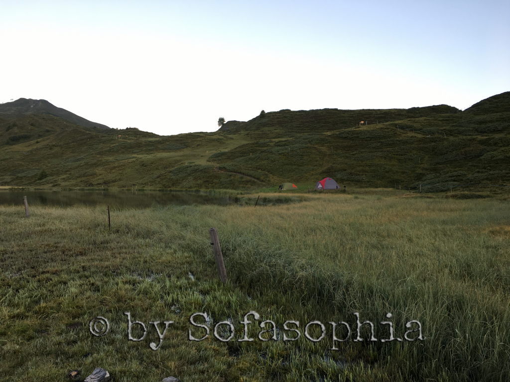 Blick von unten auf den See, den Hügel darum und das Zeltlager mit unserm Zelt und dem unserer beiden Nachbarinnen.
