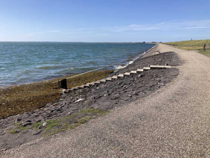 Meer und Radweg, in der Bildmitte eine Treppe, die direkt ans Meer führt.