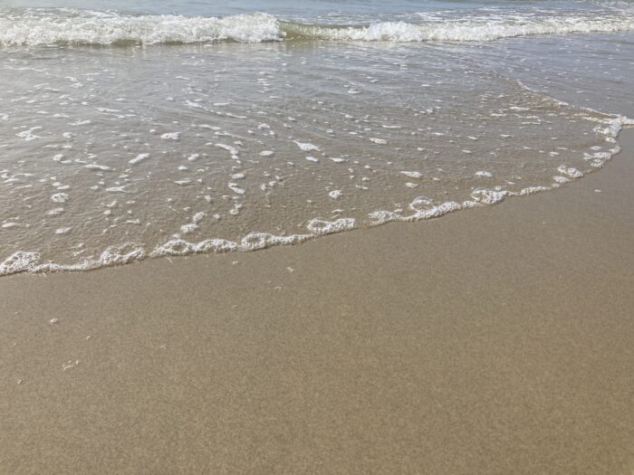 Nasser Sand und eine anrollende Meereswelle.