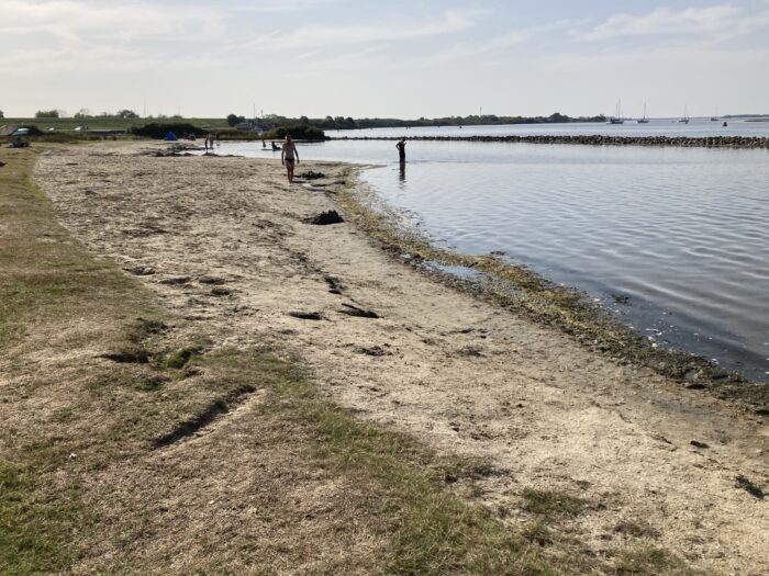Sandstrand links, Meer rechts. Wenige entfernte Menschen im und außerhalb des Wassers.