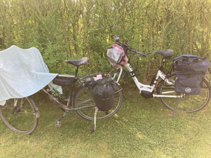 Zwei Fahrräder, auf dem linken Rad ein Tuch zum Trocknen. Beide Räder haben Radtaschen. Sie stehen vor einer Hecke auf Rasen.
