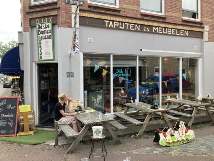 Straßenszene. Tische und Bänke vor einem Ladenlokal, das als Pfannkuchenrestaurant erkennbar ist.