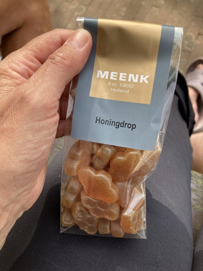 Eine linke Hand hält eine durchsichtige Packung mit Meenk-Honingdrops. Die Drops im Beutel sehen wabenförmig aus, sind honigfarben und etwa drei Zentimeter lang.