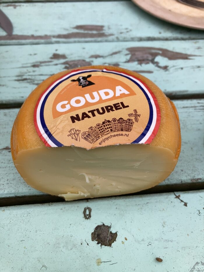 Ein runder Laib Gouda Naturel, angeschnitten, auf dem Holztisch liegend.