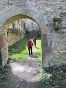 Torbogen, der auf ein ummauertes Wiesenstück führt, darin zwei Menschen, die nach oben schauen