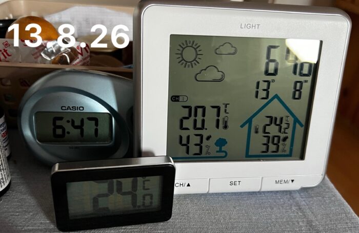 Das Bild zeigt einen Wecker, eine Wetterstation mit Uhr und ein Thermometer. Die Uhren zeigen die Uhrzeiten 6:46 und 6:47 an, während die Wetterstation Temperaturen von 20,7 °C (innen) und 24,2 °C (außen) anzeigen. Die Luftfeuchtigkeit beträgt innen 39 % und außen 43 %. Oben links ist das Datum eingeblendet: 13. 8. 26