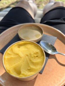 Becher mit Mangoeis auf Teller, auf Beinen, auf Liege, im HIntergrund Weitblick