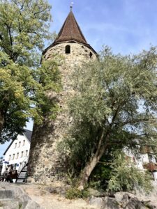 Runder Steinturm von unten vor blauem Himmel, umgeben von Bäumen rechts und links