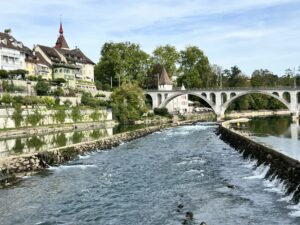 Flusskanal fließt an einer Stadt mit einer Brücke und historischen Gebäuden vorbei. Rechts und links drückt das Wasser des angrenzenden Flusses in den Kanal