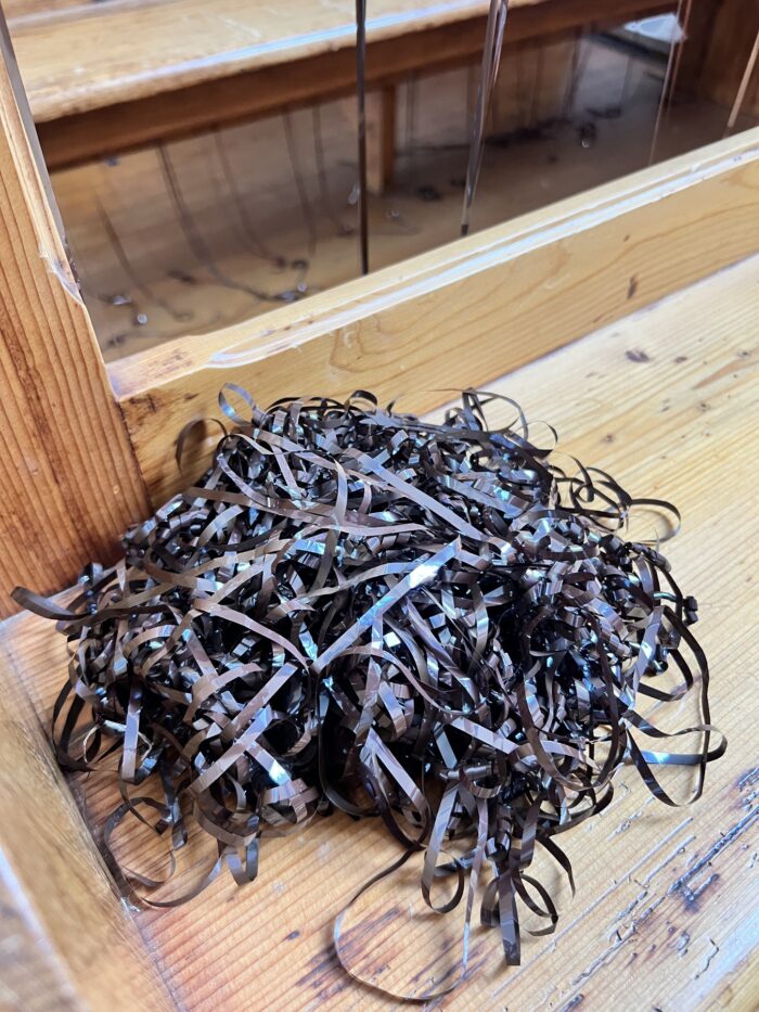 Ein Knäuel Bandsalat aus einer alten Tonbandkassette auf einer Holzbank liegend, Nahaufnahme